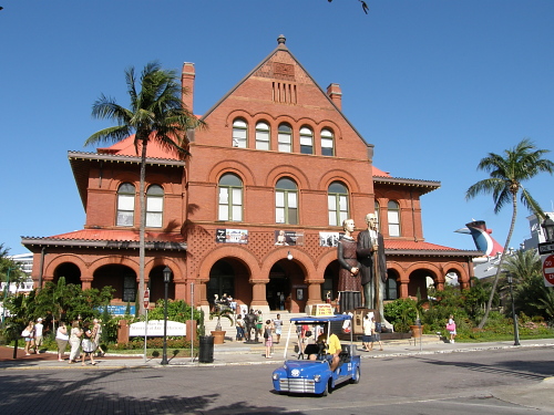 key west customs house in full glory the red brick facade dominating the street with people casually about shooting snapshots and strolling with a blue kit electric car turning around the outdoor lobby
