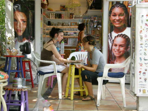 two young women casually dressed sitting in a t-shirt shop door open to the street one girl doing the nails of the other both smiling and talking