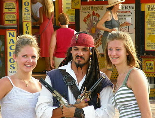 two young women at the pier flanking a busker dressed as a pirate from Pirates of the Caribbean both girls smiling
