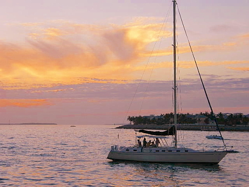 sailboat sitting on the calm waters framed by a post sunset blissful sky of pinks purples blues a small island in the background